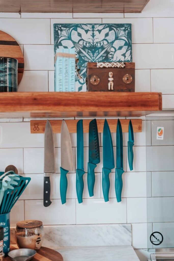 Best Kitchen Knives A set of vibrant blue kitchen knives hanging on a wooden strip in a modern kitchen setting.